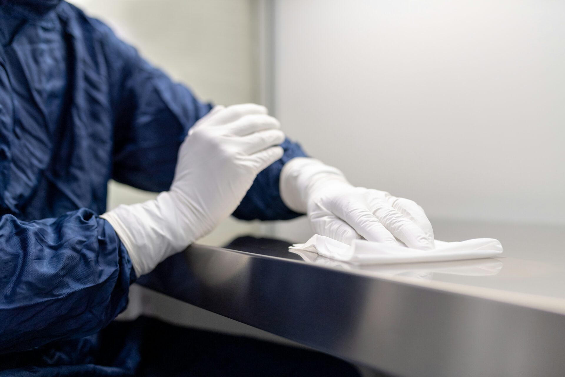 A janitor in blue overall and gloves wiping a steel slab with a cloth