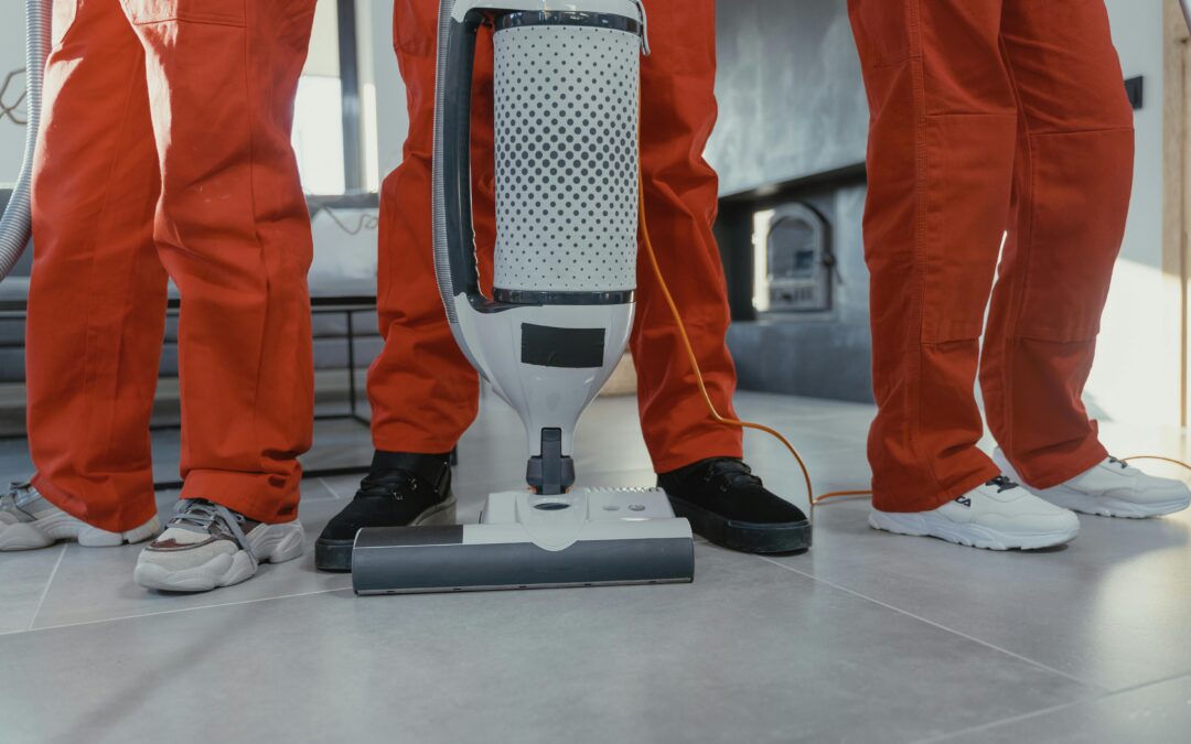 Three janitors standing while the middle one holds a white vacuum cleaner in hand